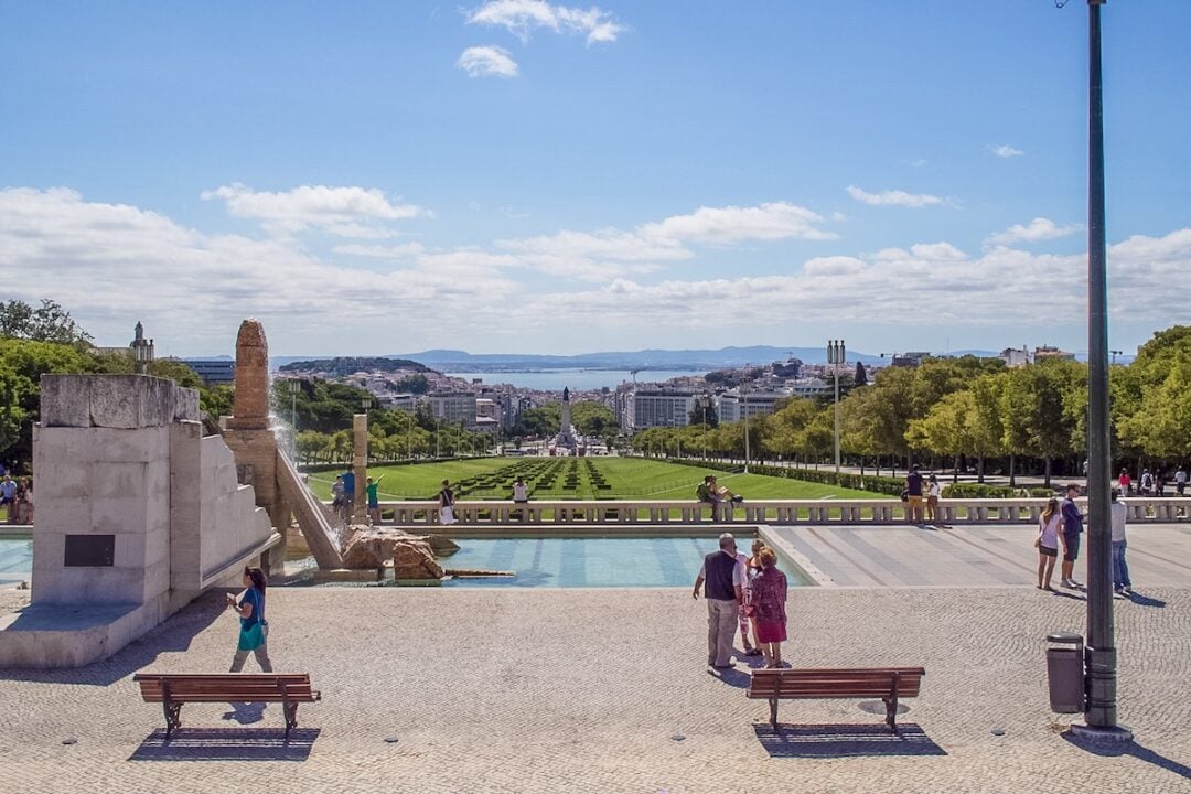 From Jardim Amália Rodrigues in Avenidas Novas, near Miradouro do Parque Eduardo VII, we can see Parque Eduardo VII leading to the Marquis of Pombal statue. Beyond it, Avenida da Liberdade stretches into Lisbon’s historic center, with the Tagus River in the background. Across the river, we can see Barreiro on the left and Seixal on the right.