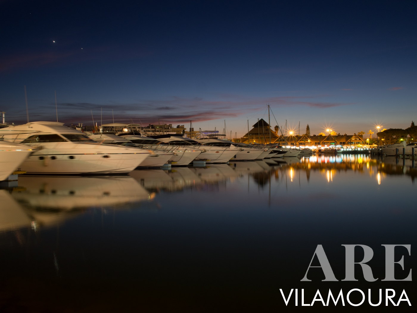 <em>Vilamoura Marina lights and reflections</em><br>Tranquil evening atmosphere at summer Vilamoura Marina, a calm picture as yachts on the placid waters, a beautiful reflection that mirrors the vibrant scene illuminated by the inviting glow from ice cream parlors, stores, pubs, and restaurants.
